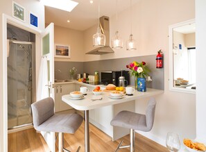 A modern kitchen with a dining area, including a glass shower, a coffee maker, and a vase with flowers. - The Hideaway (Porthleven)
