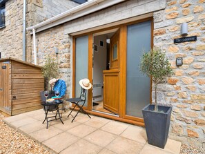 A stone building with a wooden door, a sign reading 'The Hideaway,' and a patio with a table, chairs, and a potted plant. - The Hideaway (Porthleven)