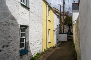 A narrow alleyway with buildings painted white and yellow, a stone wall, and a person standing at the end.