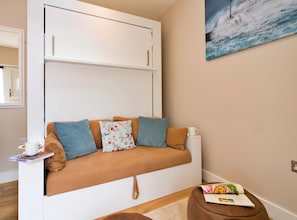 A compact living space with a sofa, cushions, a side table, a magazine, and a painting of a seascape.