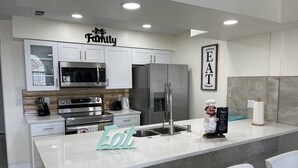 A modern kitchen with white cabinets, stainless steel appliances, a marble backsplash, and a central island with seating. - Grand Luxury Bay 3BR Penthouse near Disney (Kissimmee)