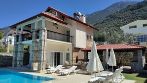 A two-story building with a swimming pool, lounge chairs, and a mountainous backdrop. - Villa Ayshella , Luxury Ovacik Villa with stunning mountain views and sunsets (Ovacık)