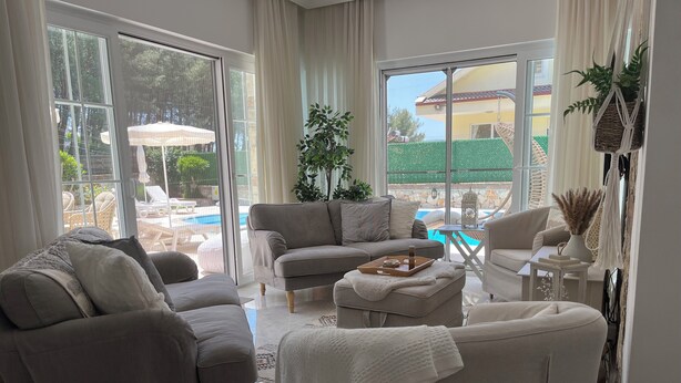 A spacious living room with a large sliding glass door leading to a pool area. There are two sofas and a coffee table with a tray. - Villa Ayshella , Luxury Ovacik Villa with stunning mountain views and sunsets (Ovacık)
