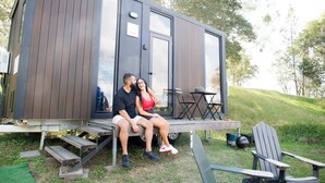 A couple sitting on a bench outside a modern, wooden cabin with a small deck and outdoor seating area.