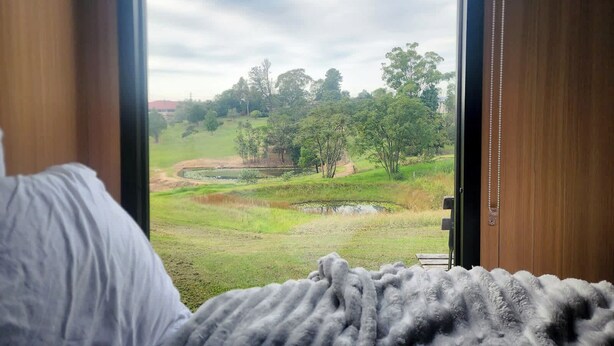 A bedroom with a large window offering a view of a grassy area with trees and a pond.