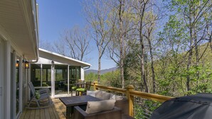 A covered outdoor patio with wicker furniture and a glass door leading to a seating area. - Grey Eagle Lodge | Pet Friendly, Deck & Game Room 10 Min. from Black Mtn (Black Mountain)