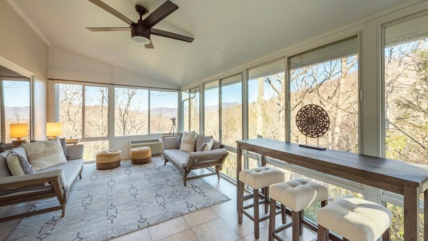 A sunroom with a ceiling fan, large windows, a sofa, a coffee table, and a bar area with stools. - Grey Eagle Lodge | Pet Friendly, Deck & Game Room 10 Min. from Black Mtn (Black Mountain)
