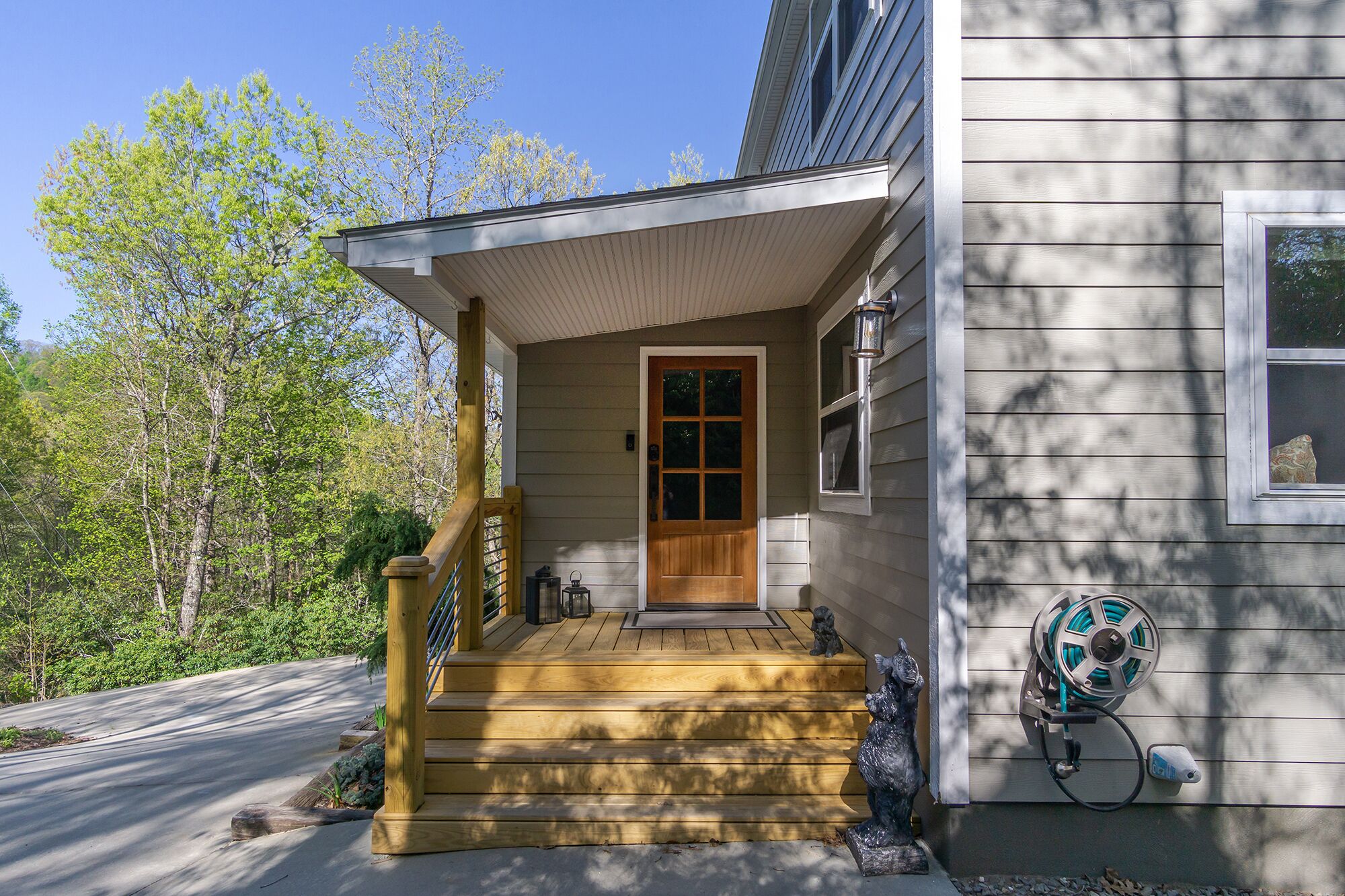 A house with a wooden front porch, a front door, and a garden hose mounted on the wall.
