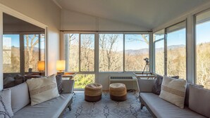 A sunlit room with a large window, a sofa with cushions, a rug, and a tripod with a camera. - Grey Eagle Lodge | Pet Friendly, Deck & Game Room 10 Min. from Black Mtn (Black Mountain)