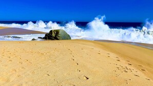 Ein sandiger Strand mit Fußspuren und einem großen Felsen im Vordergrund.