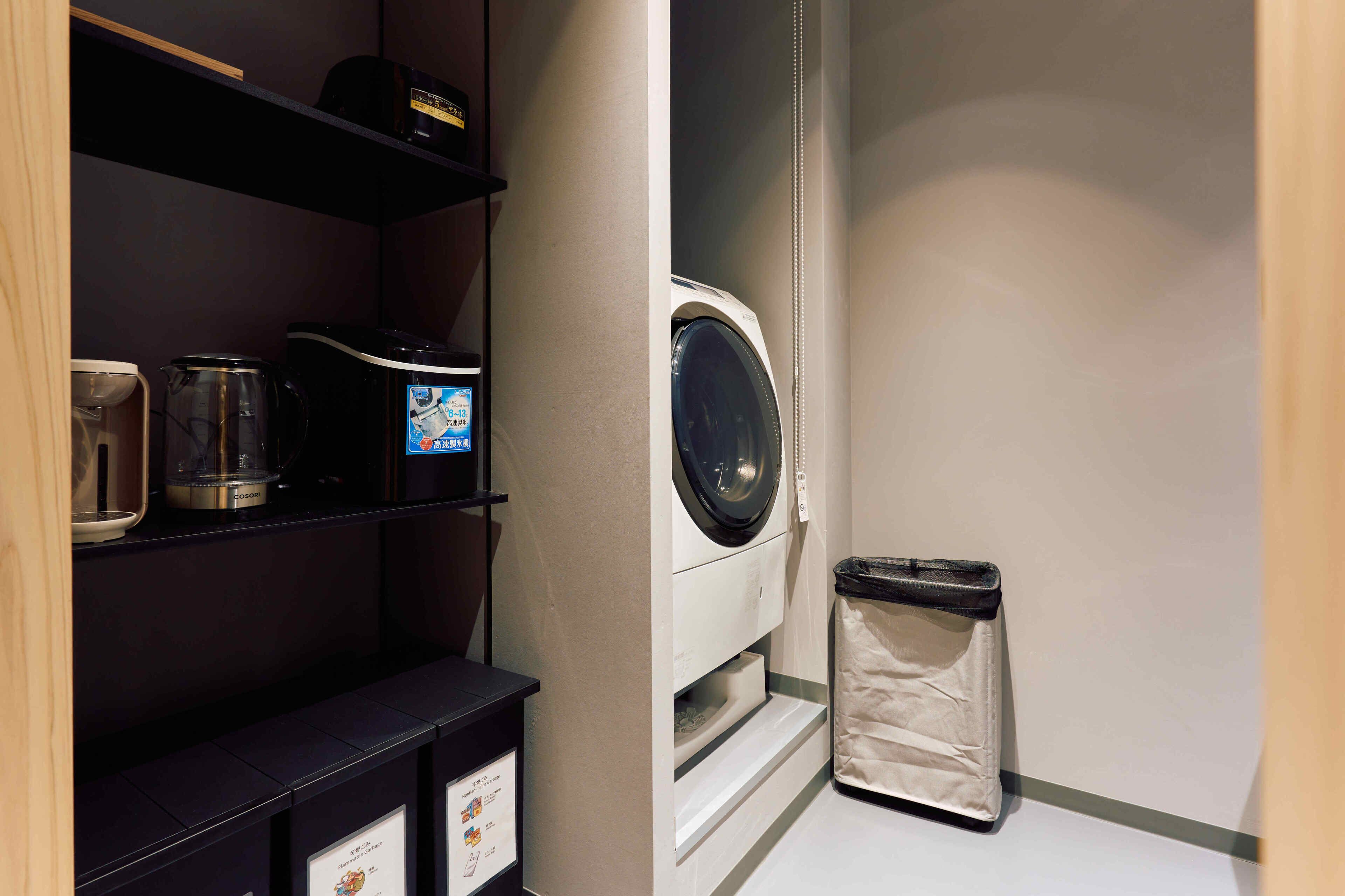 A laundry area with a washing machine, a trash bin, and a coffee maker on a shelf.