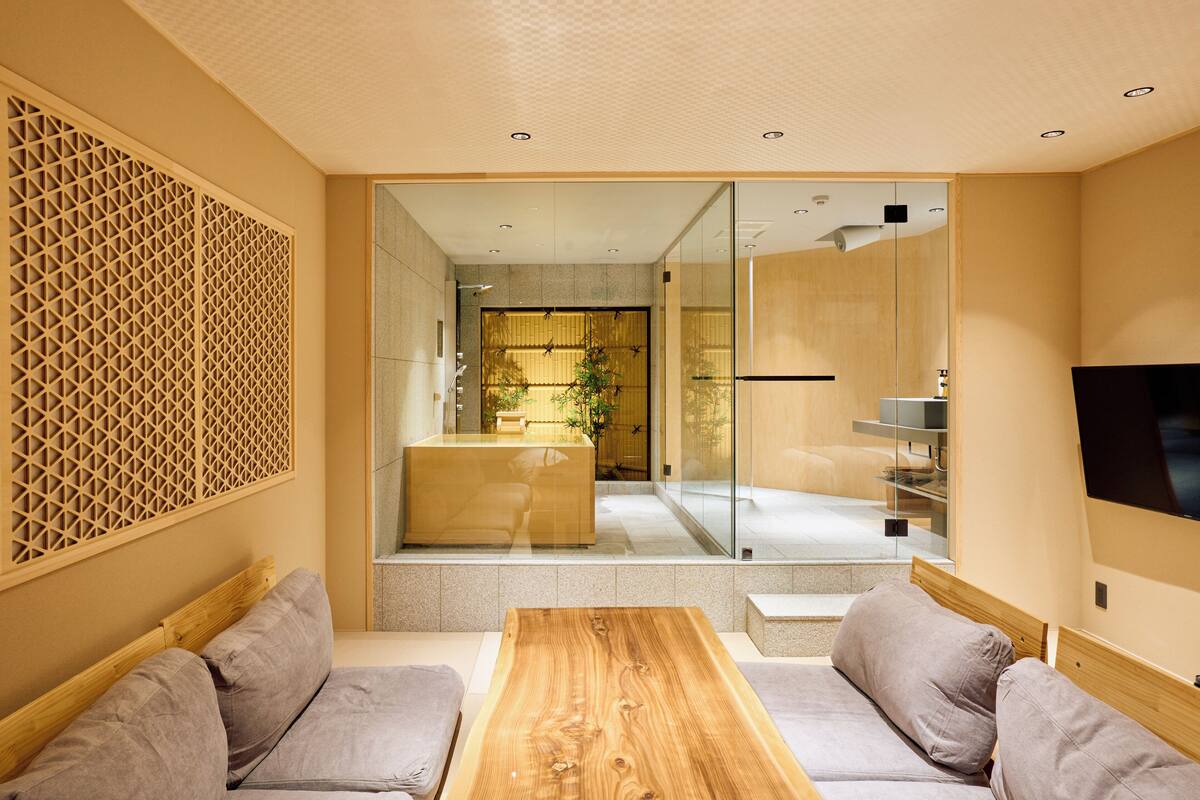 Un salón moderno con una mesa de centro de madera, sofás grises y un separador de vidrio que da a una zona de cocina.