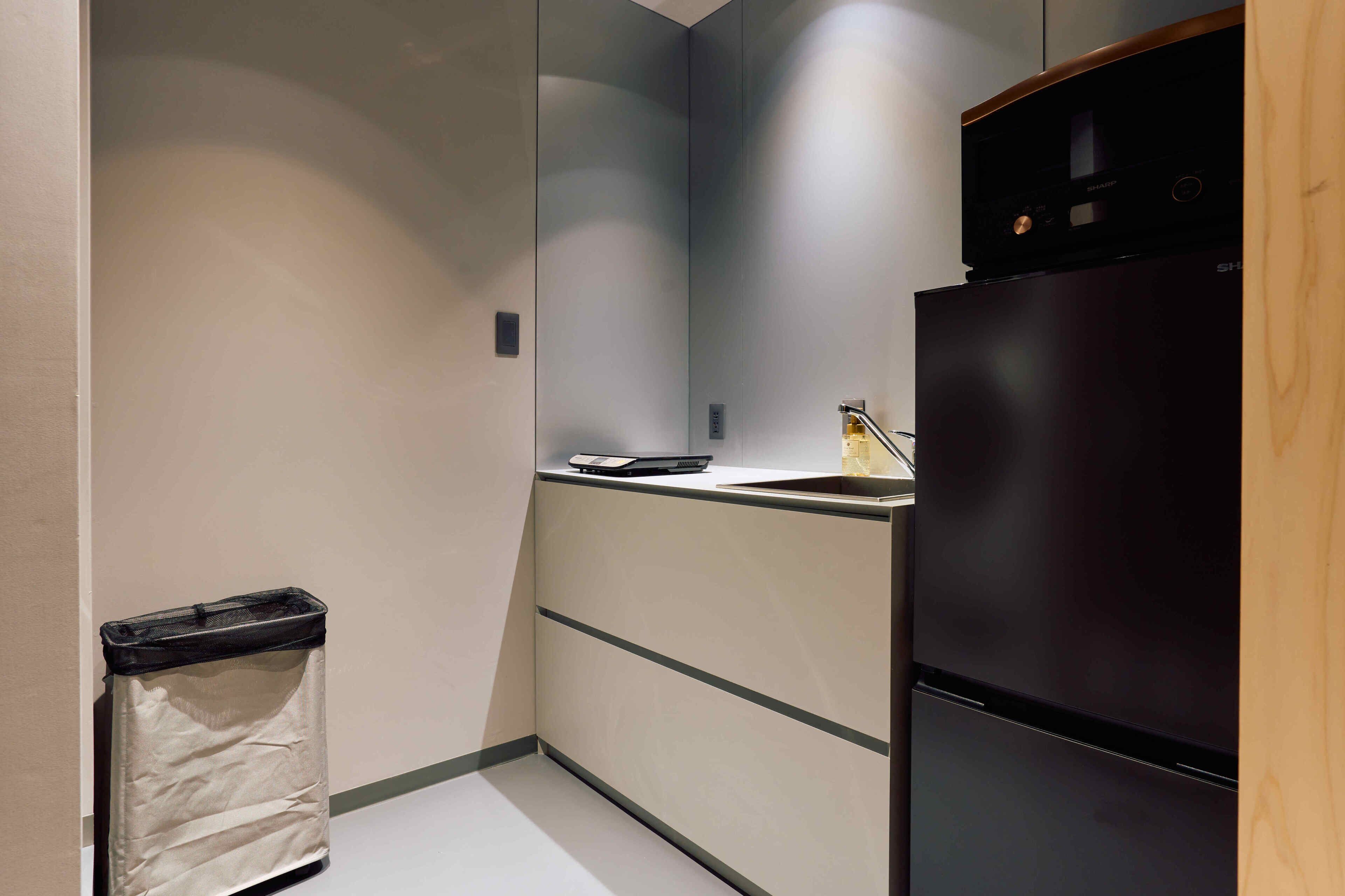 A compact kitchen with a black refrigerator, a small countertop, and a trash bin.