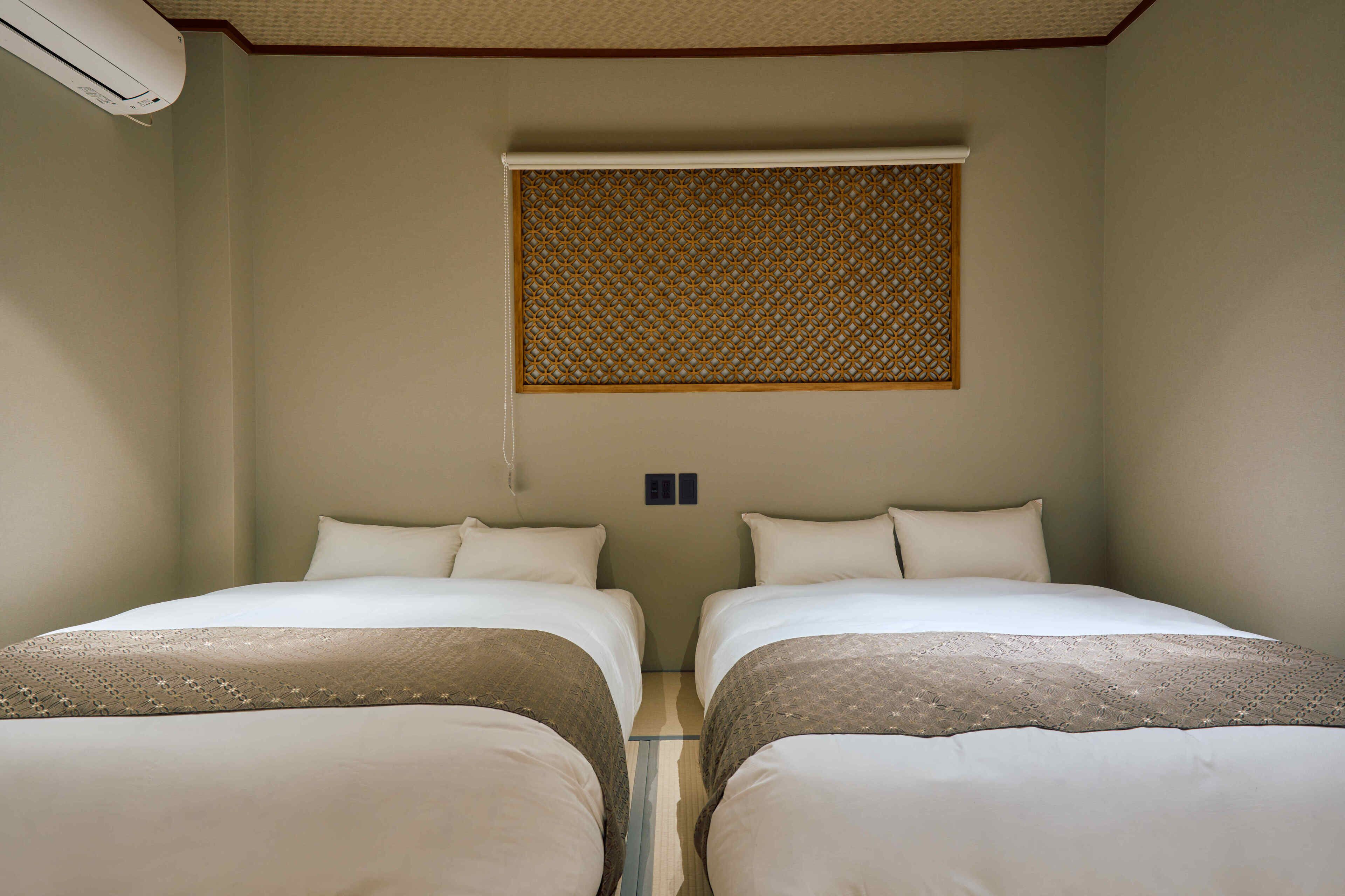 Habitación de hotel con dos camas, una ventana con un panel decorativo y un equipo de aire acondicionado.