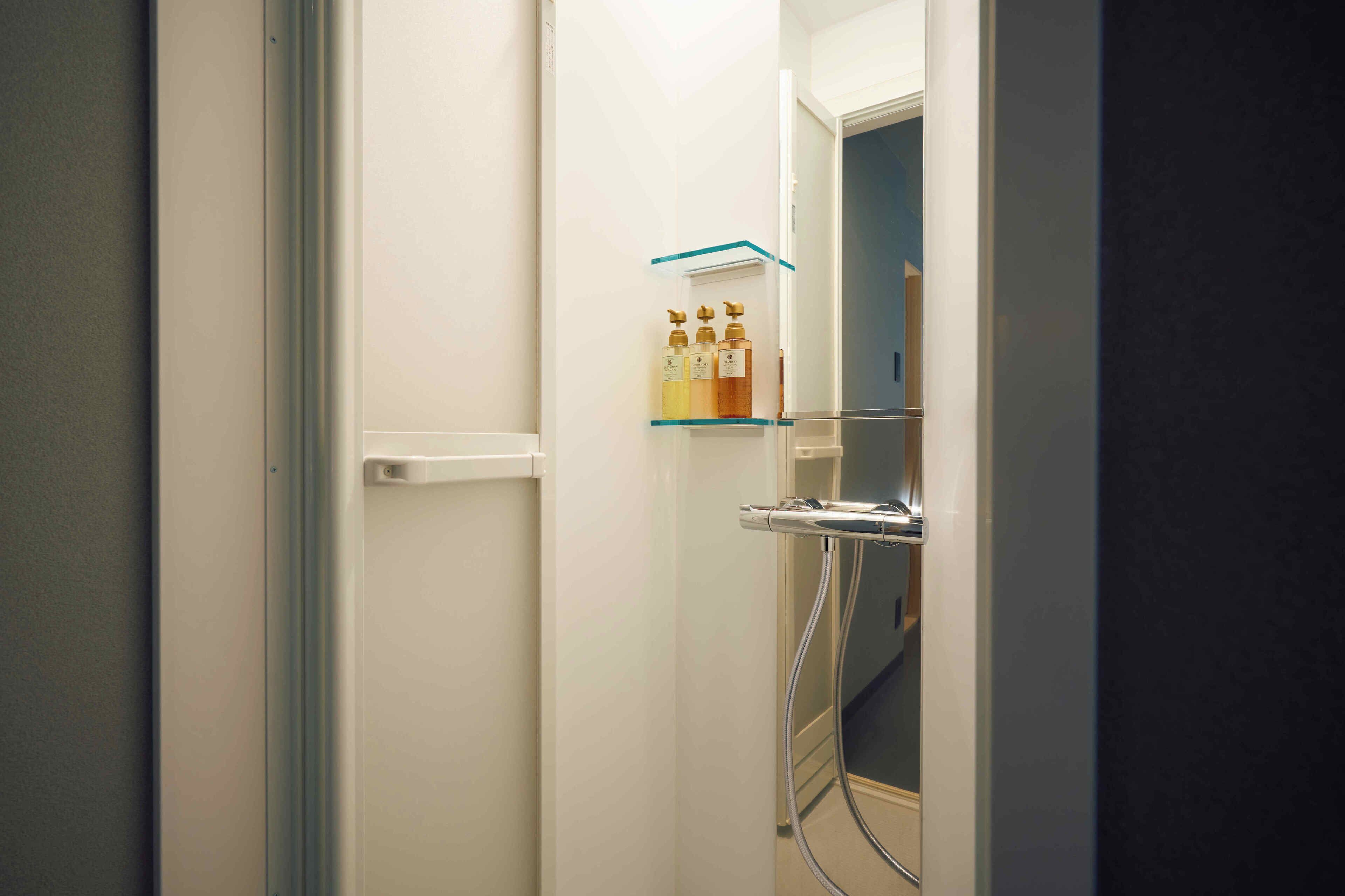 Ein Badezimmer mit einer Glastrennwand, Ablage für Toilettenartikel, einer Duschkabine und einer Tür mit weißem Griff.