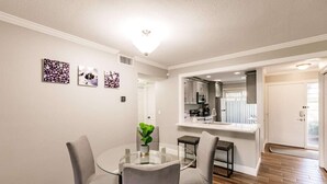 A modern dining area with a glass table and cushioned chairs, a kitchen with a large island, and a wooden floor.