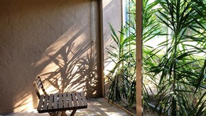 A wooden bench in a sunlit room with a ceiling fan and a view of greenery through large windows.