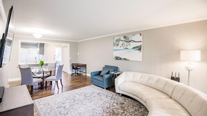 Un salon moderne avec un canapé blanc aux lignes courbes, un fauteuil bleu et un coin repas comprenant une table et des chaises en verre.