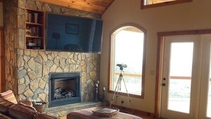A cozy living room with a stone fireplace, leather sofa, and a ceiling fan.