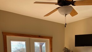 A bedroom with a bed, a ceiling fan, a wooden dresser, and a TV on the wall.
