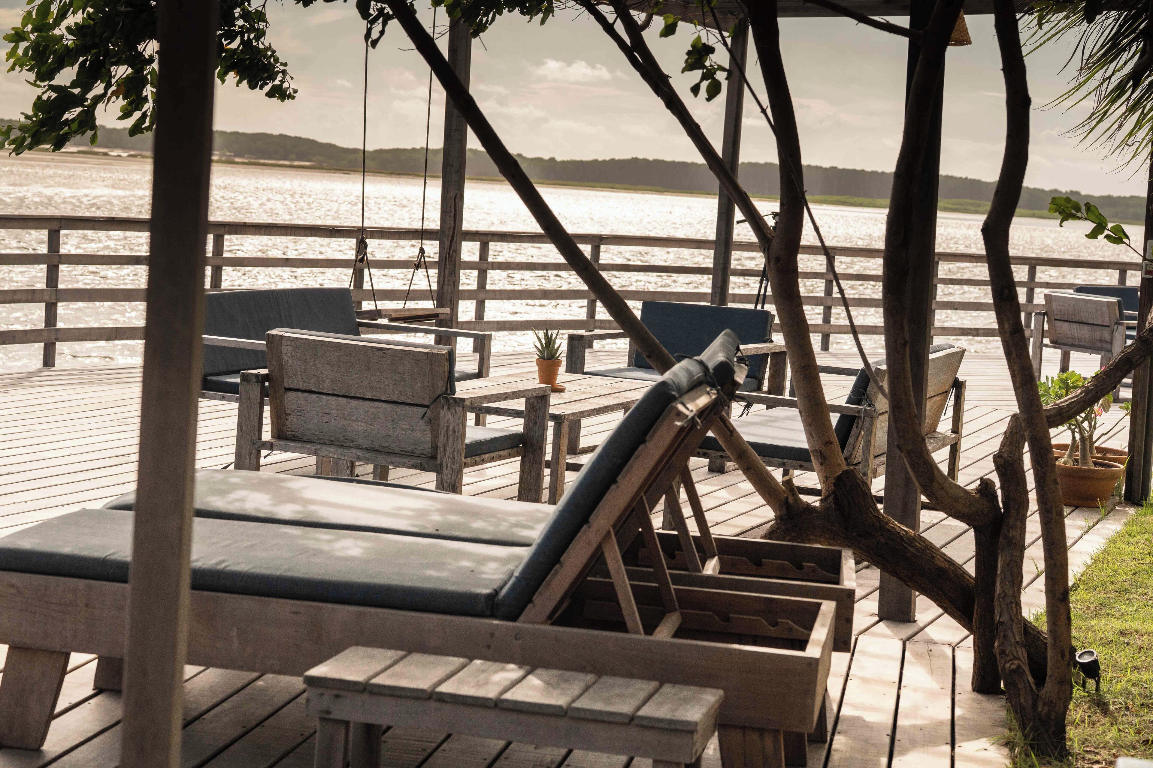 A wooden deck with lounge chairs and tables overlooking a body of water.