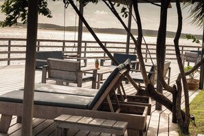 A wooden deck with lounge chairs and tables overlooking a body of water.