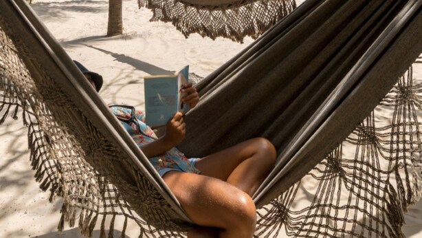 A hammock on a sandy beach with palm trees and a yellow vehicle in the background.