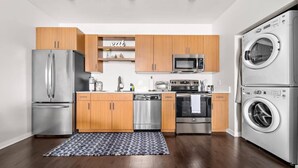 A modern kitchen with stainless steel appliances, wooden cabinets, and a built-in washing machine. - TC Condo | Steps to Tart Trail | Near Downtown (Traverse City)
