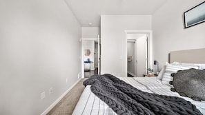A bedroom with a large bed, a dark throw blanket, and a headboard. There is a door leading to another room.