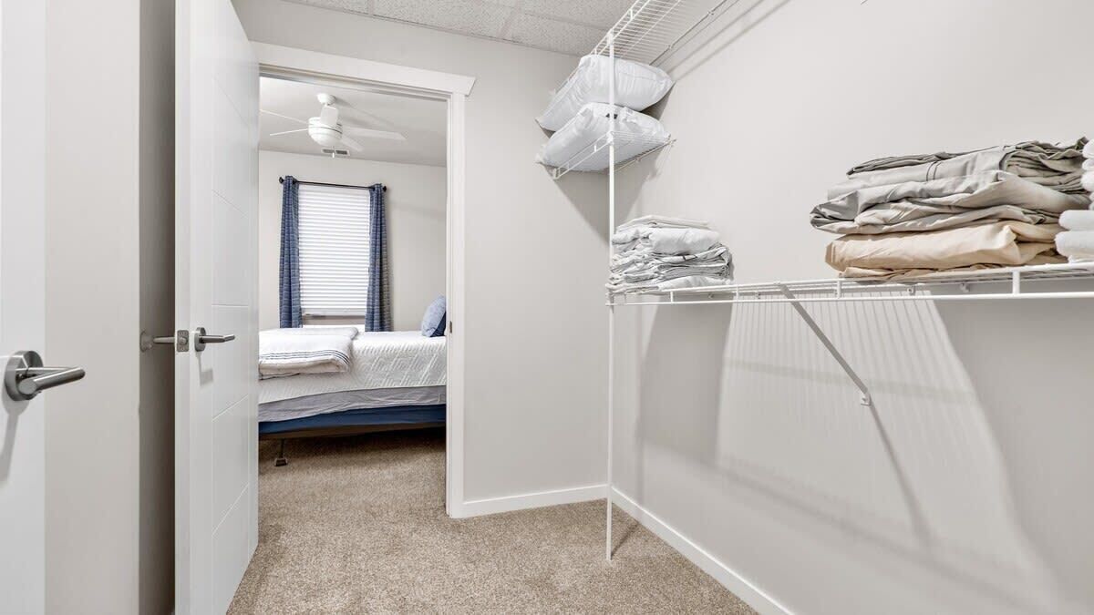 A bedroom with a bed, a closet with folded clothes, and a door leading to another room.