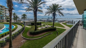 Un espace piscine aménagé dans un complexe hôtelier, avec des palmiers, un élément décoratif aquatique et une vue sur le port de plaisance.