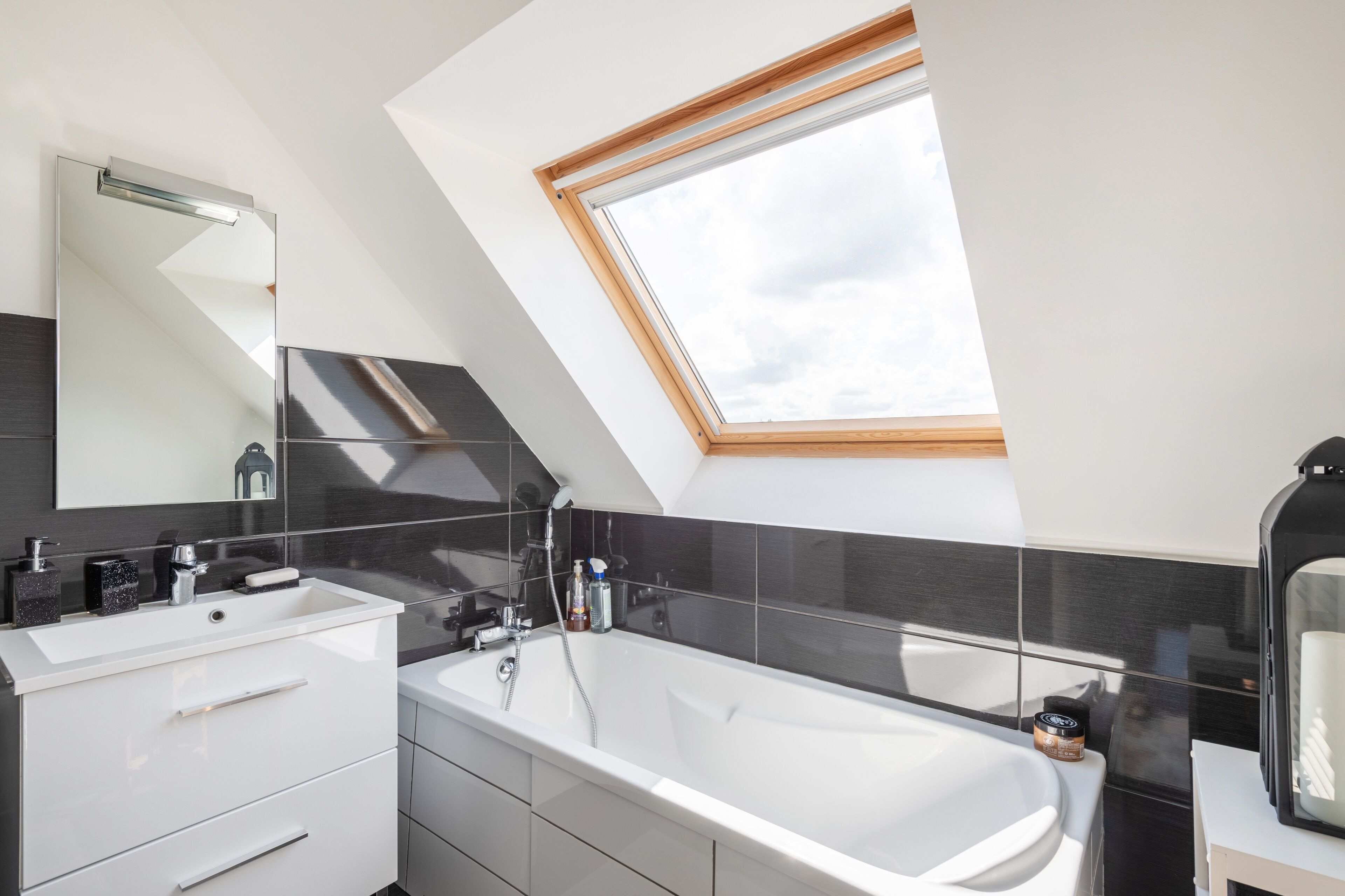 Een moderne badkamer met dakraam, een ruime badkuip en een wastafel met lades.