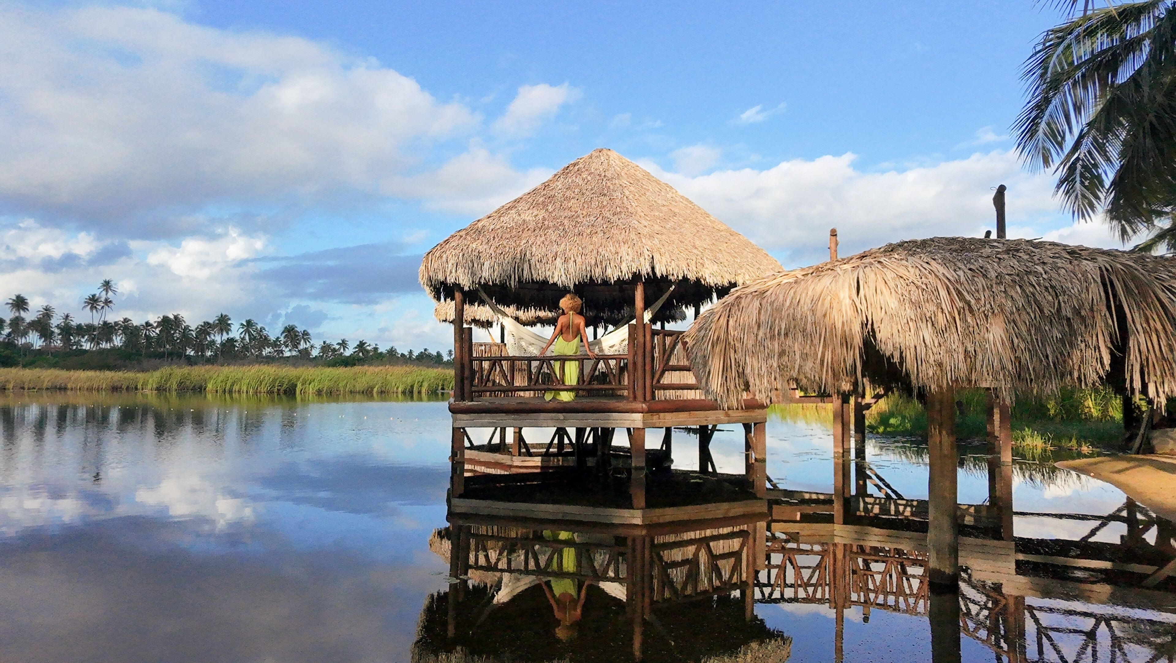 A thatched-roof structure over water, with a person standing on it.
