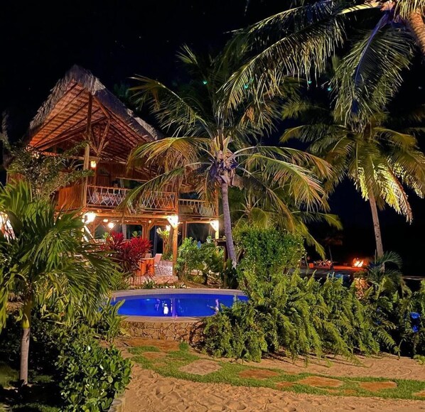 A two-story building with a thatched roof, surrounded by palm trees and a swimming pool. - Moriá Eco Lodge (Amontada)