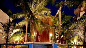 Una entrada de resort bien iluminada, con palmeras y una escalera que conduce al edificio principal.