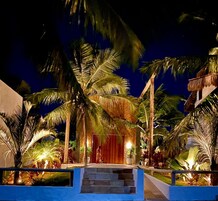 Entrada iluminada do resort, com palmeiras e uma escadaria que leva ao edifício principal.