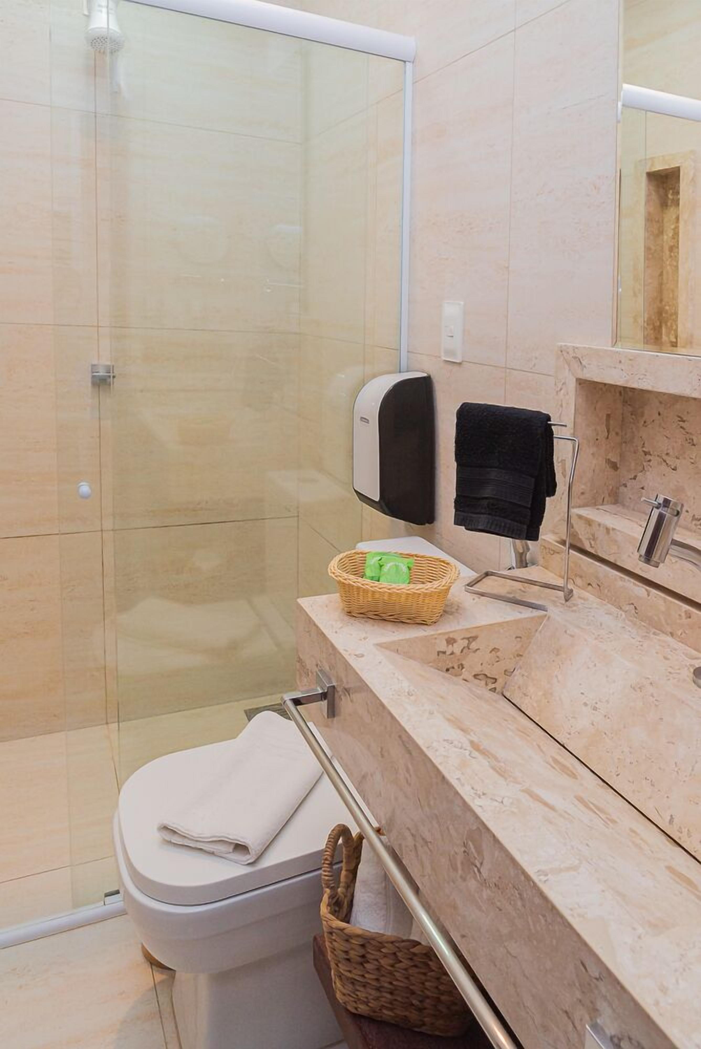 Un baño moderno con cabina de ducha de vidrio, inodoro con toalla, lavamanos con dispensador de jabón y espejo.