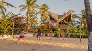 Partido de voleibol de playa en una cancha arenosa rodeada de palmeras y una estructura con techo de paja.