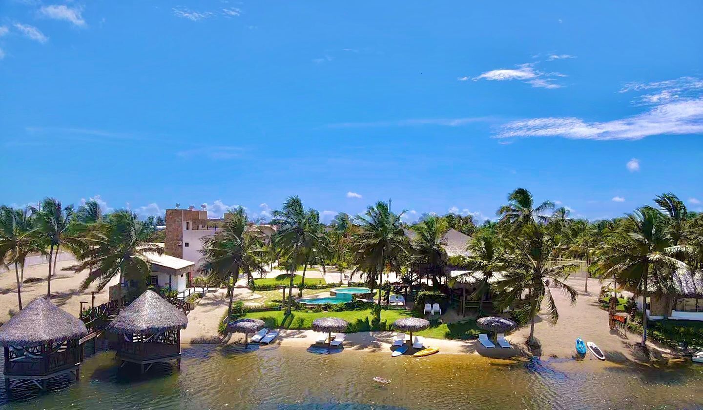 A resort with thatched-roof cabanas, a pool, and palm trees.