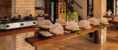 Un coin cuisine avec une colonne en briques, une cuisinière et une table en bois sur laquelle se trouvent des aliments couverts.