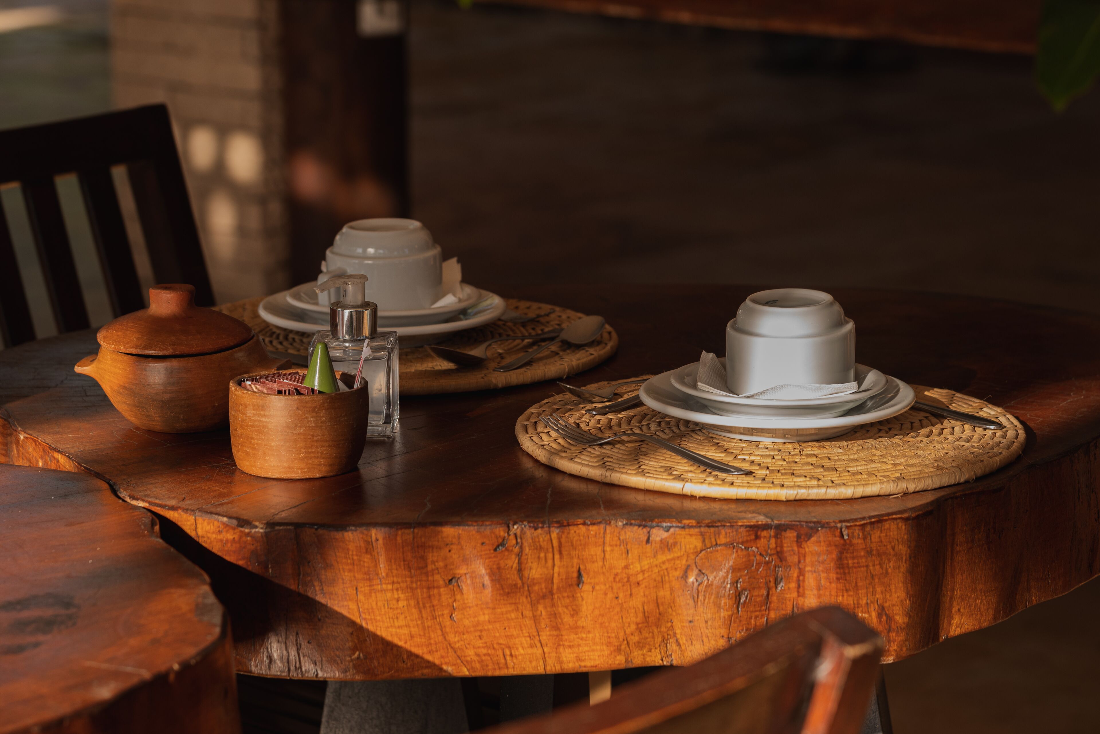 A wooden table with a woven placemat, a clay pot, and a glass container with a green plant.