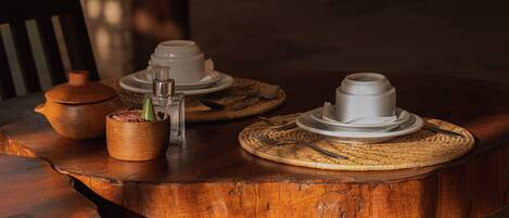 A wooden table with a woven placemat, a clay pot, and a glass container with a green plant.