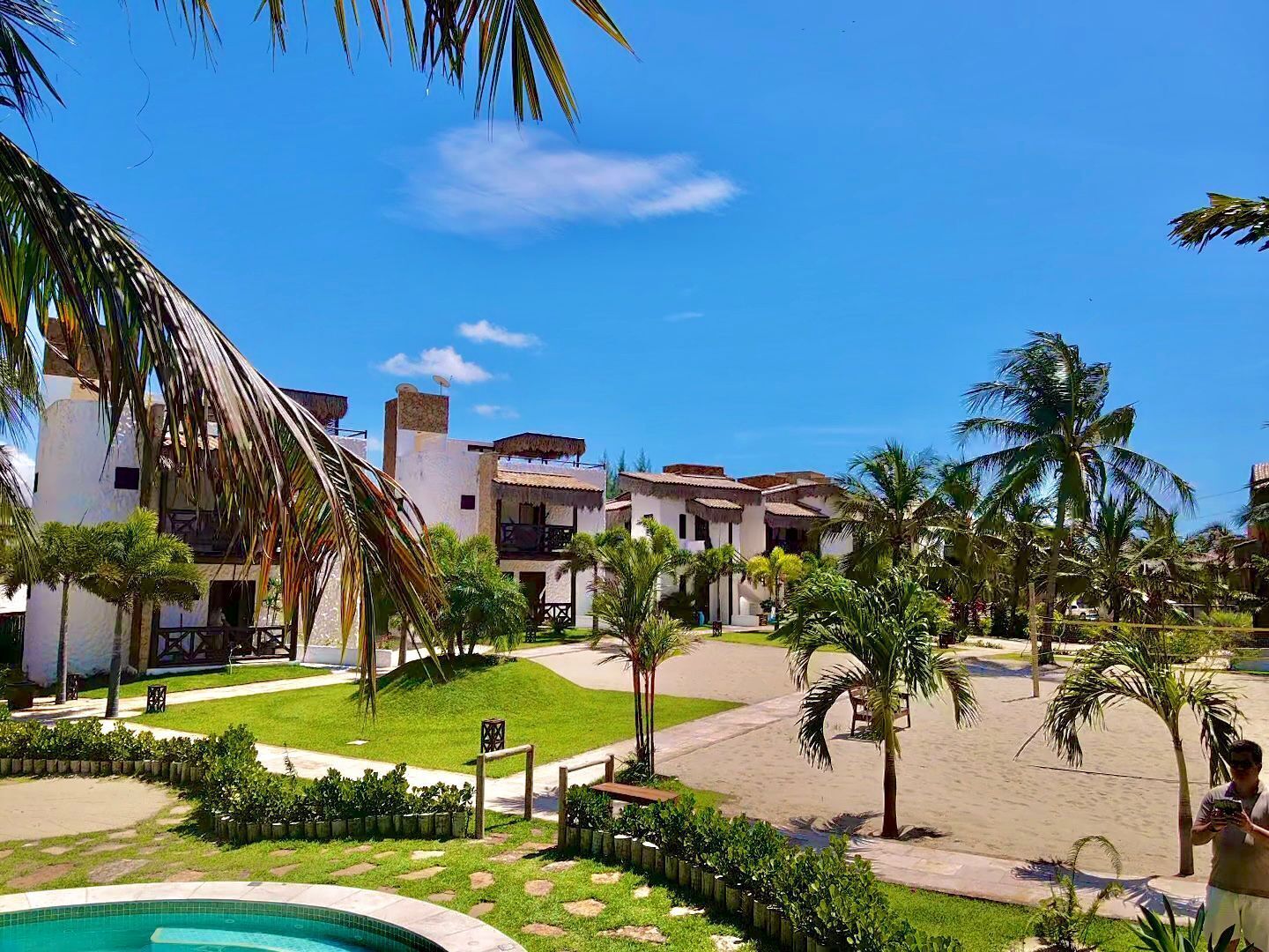 Un resort con varias edificaciones blancas, una piscina y palmeras.