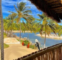 Vista para a praia com palmeiras, piscina e uma prancha de surf.