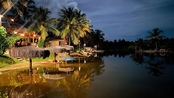 A calm water body reflecting palm trees and a thatched-roof structure.