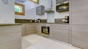 A modern kitchen with a built-in oven, stainless steel cabinets, a window, and a clock on the wall. - Altaka 5 - Beautiful 2 bedrooms apartment (MORZINE)