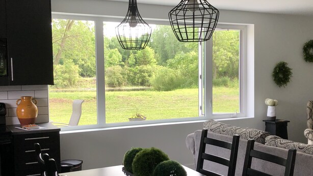Un espace repas comprenant une table et des chaises, une fenêtre donnant sur un paysage verdoyant et des luminaires suspendus.