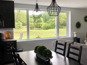 Un comedor con una mesa y sillas, una ventana con vistas a follaje e iluminación colgante.