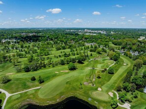 Vue aérienne d’un parcours de golf avec plusieurs greens, des bunkers de sable et un lac au premier plan.