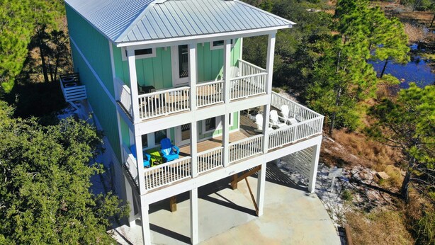 A two-story house with a balcony, surrounded by trees and a body of water.